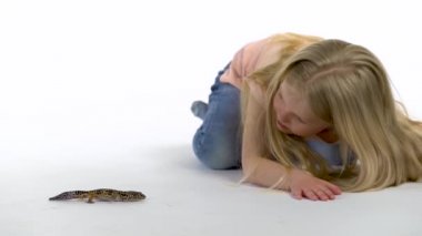 Uzun sarı saçlı küçük kız beyaz arka planda leoparın yanında oturuyor. Yavaş çekim