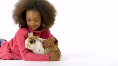 Küçük Afrikalı kıvırcık kız beyaz arka planda üç renkli tavşana sarılıyor. Yavaş çekim