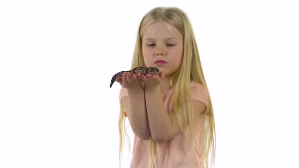 La bambina con lunghi capelli biondi tiene il leopardo eublefar su sfondo bianco. Rallentatore — Video Stock