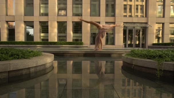 Hermosa joven bailando en la calle de una ciudad moderna y se refleja en el agua. Movimiento lento — Vídeo de stock