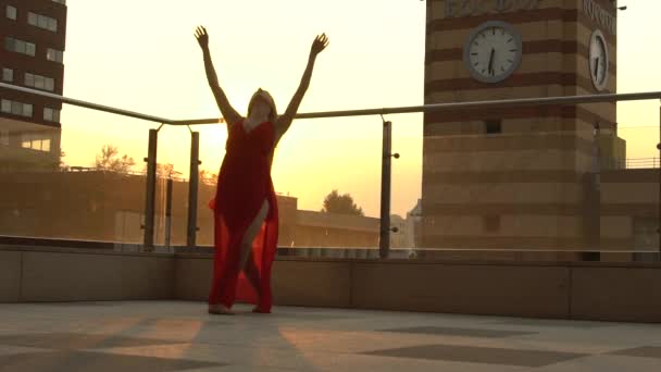 Menina bonita dançando na rua de uma cidade moderna sob a luz do sol. Ela está usando um vestido vermelho. Movimento lento . — Vídeo de Stock