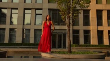 Modern bir şehrin caddesinde dans eden güzel genç kız suya yansıyor. O kırmızı bir elbise giyiyor. Yavaş çekim.