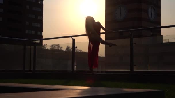 Silhouette Schöne junge Frau tanzt auf der Straße einer modernen Stadt im Sonnenuntergang. Sie trägt ein rotes Kleid. Zeitlupe. — Stockvideo