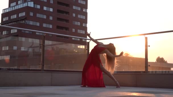 Menina bonita dançando na rua de uma cidade moderna sob a luz do sol. Ela está usando um vestido vermelho. Movimento lento . — Vídeo de Stock