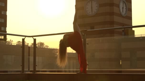 Schöne junge Mädchen tanzen auf der Straße einer modernen Stadt im Sonnenuntergang. Sie trägt ein rotes Kleid. Zeitlupe. — Stockvideo