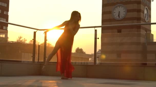 Hermosa joven bailando en la calle de una ciudad moderna a la luz del atardecer. Lleva un vestido rojo. Movimiento lento . — Vídeo de stock