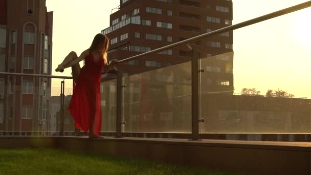 Prachtig jong meisje dansend op de straat van een moderne stad in het zonsondergang licht. Ze draagt een rode jurk. Langzame beweging. — Stockvideo