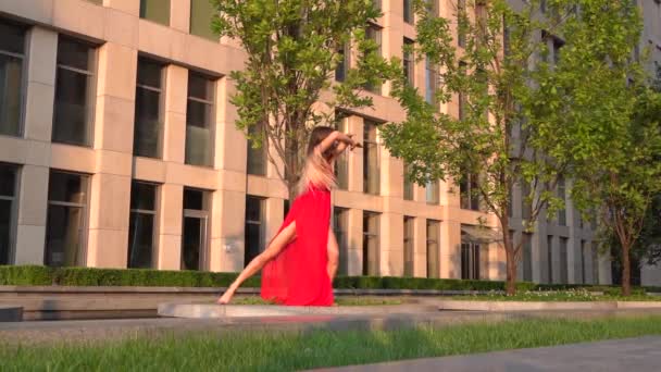 Menina bonita dançando na rua de uma cidade moderna e se reflete na água. Ela está usando um vestido vermelho. Movimento lento. — Vídeo de Stock