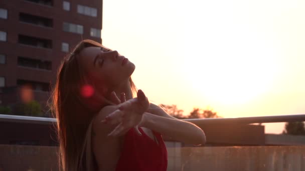Vacker ung flicka dansar på gatan i en modern stad i solnedgången ljus. Hon bär en röd klänning. Långsamma rörelser. — Stockvideo