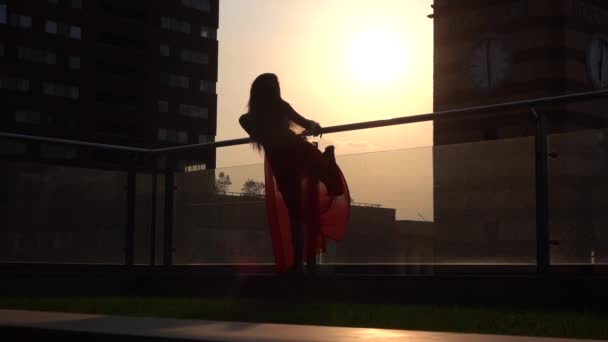 Günbatımında modern bir şehrin sokaklarında dans eden güzel genç kız. O kırmızı bir elbise giyiyor. Yavaş çekim. — Stok video