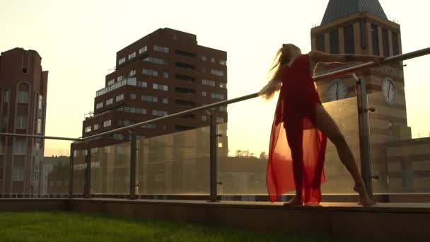 Krásná mladá dívka tančí na ulici moderního města v západu slunce. Má na sobě červené šaty. Zpomalený pohyb. — Stock video