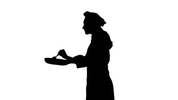 La silueta negra del cocinero en el sombrero es freír y prueba el plato. Aislado sobre fondo blanco . — Foto de Stock