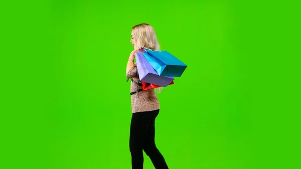 Blondes Mädchen trägt viele verschiedene Farbverpackungen. Grüner Bildschirm. Seitenansicht — Stockfoto