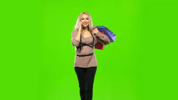 Blonde girl carries a multi colored packages, talking on the phone and smiles sweetly. Green screen — Stock Photo, Image