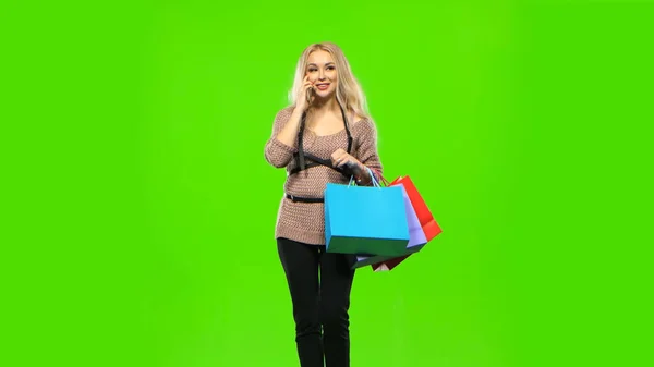 Blonde girl carries a multi colored packages, talking on the phone and smiles sweetly. Green screen — Stock Photo, Image