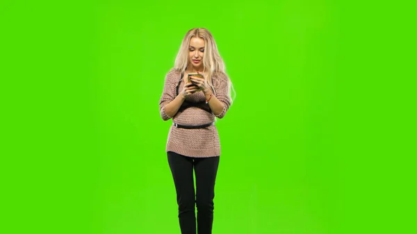 Blondine geht und schaut auf Ihr Handy. Grüner Bildschirm — Stockfoto