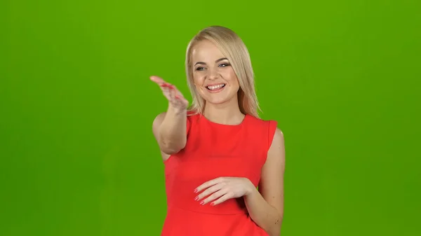 Dame in rood op groen scherm achtergrond toont haar hand kijken naar de camera — Stockfoto