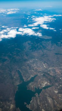 Göl ve dağların havadan görünüşü. Uçak penceresinden bak. Bulutların ve mavi gökyüzünün altında güzel bir manzara.