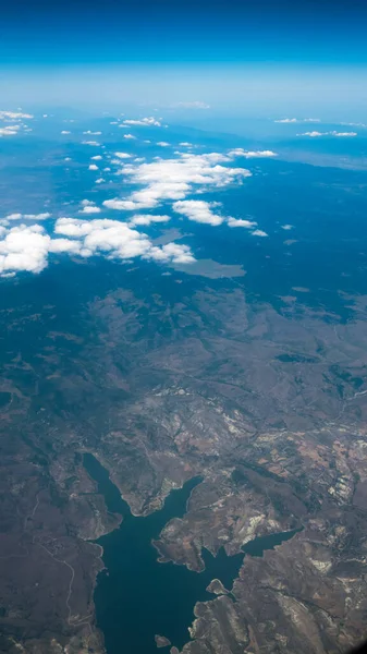 Vista aérea del lago y las montañas. Vista desde la ventana de un avión. Hermoso paisaje bajo las nubes y el cielo azul —  Fotos de Stock