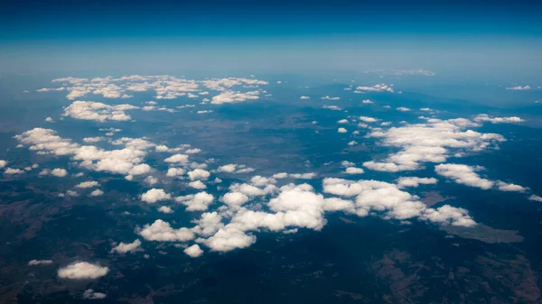 Vista aérea de las montañas bajo las nubes y el cielo azul. Vista desde la ventana de un avión. Hermoso paisaje —  Fotos de Stock