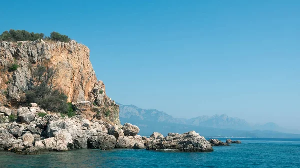 Beautiful deep sea with small waves and steep cliffs on shores of Sea with trees and caves against mountains in distance — Stock Photo, Image