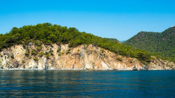 Beautiful deep sea with small waves and steep cliffs on the shores of the Mediterranean Sea with trees and caves. — Stock Photo, Image