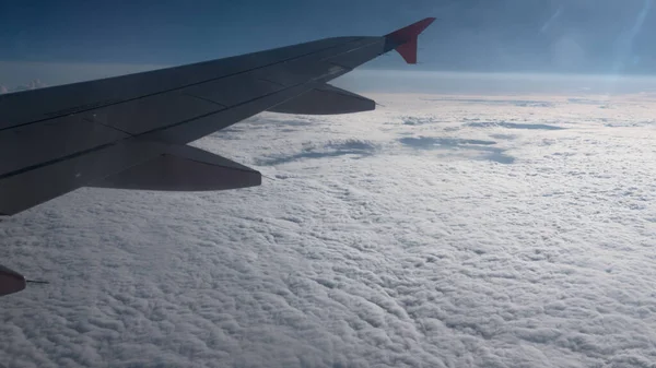 Ala de avión volando por encima de las nubes en el cielo y con una vista nubes gruesas bajo rayos soleados . —  Fotos de Stock