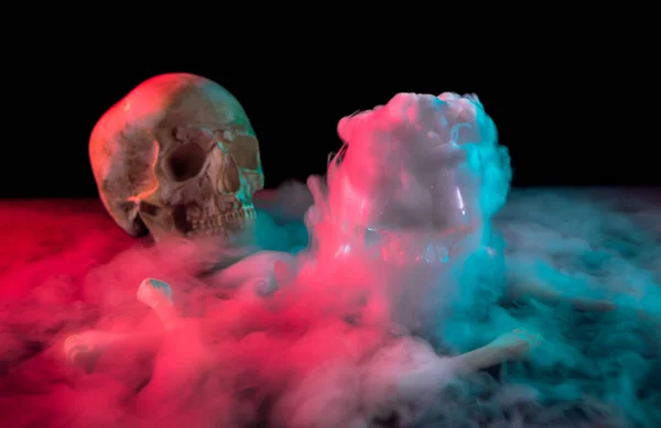 Menselijke schedel in de buurt van botten en dikke witte rook stroomt rond voor Dag van de Dood op donkere achtergrond met rood en groen licht. — Stockfoto