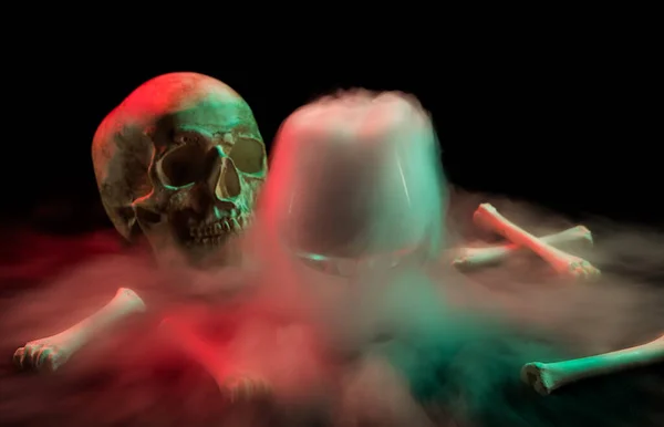 骨の近くの人間の頭蓋骨と濃い白煙が赤と緑の光を背景に死の日の周りに流れる. — ストック写真
