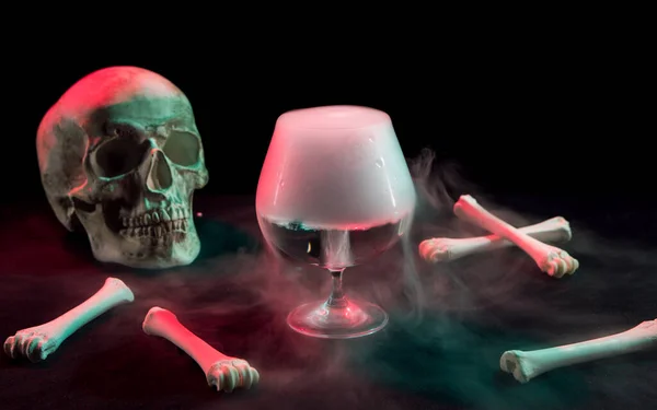 Human skull near bones and thick white smoke flowing around for Day of Dead on dark background with red and green light.