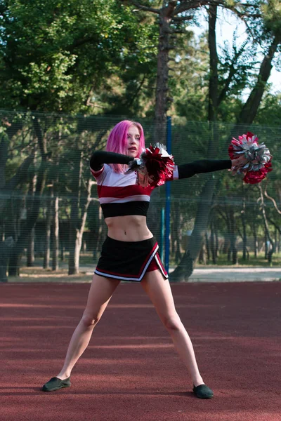 身材苗条的女子啦啦队队长，一头粉色的头发，身披红色和银色的花冠，在体育场外跳舞 — 图库照片