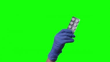 Doktor hapları gösteriyor. Korumalı mavi eldivenli kadın elleri yeşil ekrana yakın çekim yapıyor..