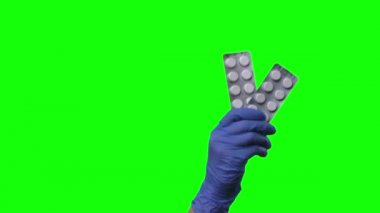 Doktor hapları gösteriyor. Korumalı mavi eldivenli kadın elleri yeşil ekrana yakın çekim yapıyor..