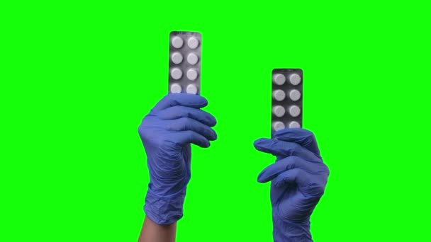 Доктор показывает таблетки. Руки женщины в защитных голубых перчатках крупным планом на зеленом экране . — стоковое видео