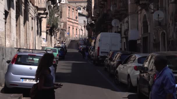CATANIA, SICILY, ITALIEN - SEPT, 2019: Smala livliga gatan i historiska centrum. Gamla byggnader med balkonger. Parkerade och flyttade bilar. Promenadturister — Stockvideo