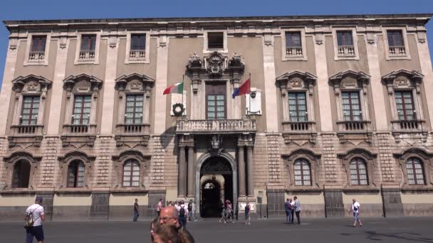 CATANIA, SICILY, ITALIË - SEPT, 2019: Olifanten paleis, stadhuis met balkon, twee vlaggen en gevel versierd door sculpturen. Wandelende toeristen — Stockvideo