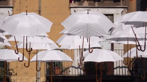 Weiße Regenschirme hängen an Seilen zwischen alten Gebäuden und wiegen sich im Wind. Umbrella Sky Project. Catania, Sizilien, Italien. Nahaufnahme