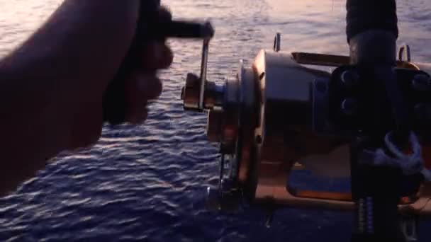 Manos de pescador sosteniendo caña de pescar, retorciendo carrete dorado. Un tipo pescando desde el barco. Ripear la superficie del agua. De cerca. — Vídeos de Stock