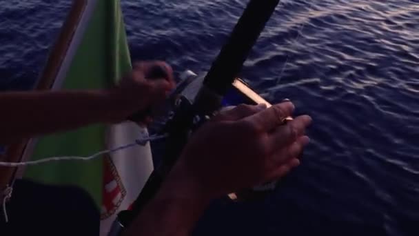 Manos de hombre sosteniendo caña de pescar, carrete giratorio. Guy pescando desde un velero con la bandera de Italia ondeando en él. Ripear la superficie del agua. De cerca. — Vídeos de Stock