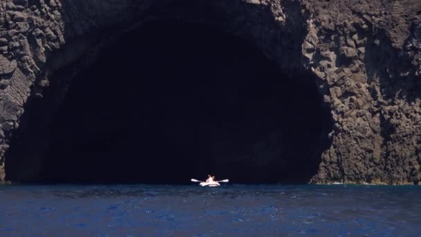 Gente en bote inflable remando remos y flotando fuera de la cueva de la isla de Lipari, mar Mediterráneo. Día soleado de verano. Sicilia, Italia — Vídeo de stock