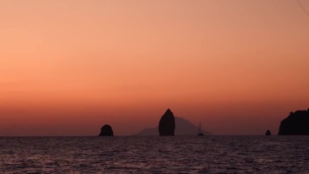 Olta ipi, yüksek kayalar ve Lipari Adaları. Akdeniz 'de yelkenli bir tekne ufka karşı. Renkli gökyüzü, gün doğumu ya da gün batımı. Sicilya, İtalya — Stok video