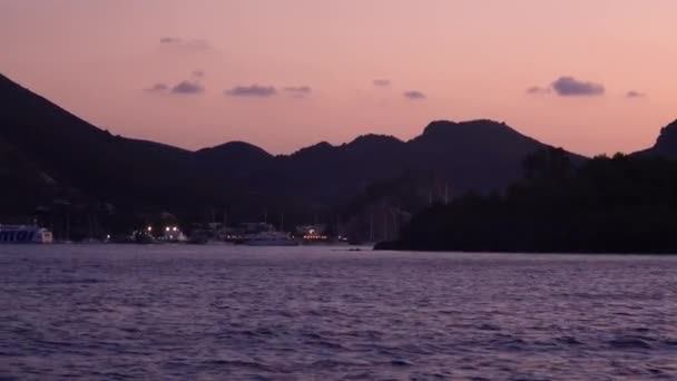 Biały statek wycieczkowy z niebieskim napisem na nim, żaglówki i jachty zacumowane na molo w Morzu Śródziemnym. Zachód słońca, góry — Wideo stockowe