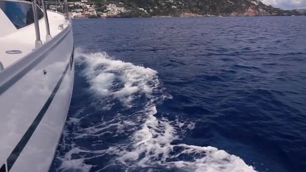 Белая яхта плавает, создавая пенные волны на поверхности моря. Липари, Сицилия, Италия. Медленное движение — стоковое видео