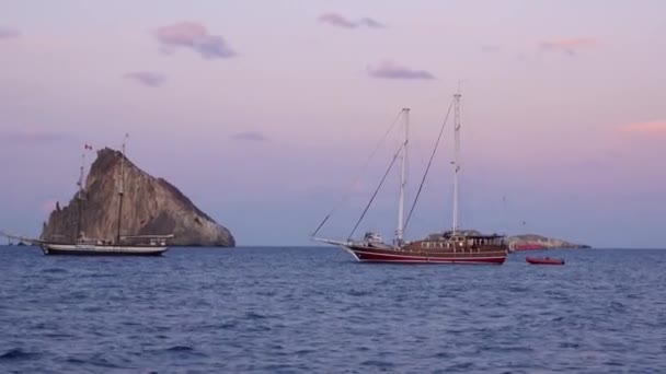 Veleiros flutuando perto de rochas no mar Mediterrâneo. Noite de verão, pôr-do-sol. Lipari Islands, Sicília, Itália — Vídeo de Stock
