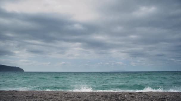 Берег моря, омываемый волнами с пеной. Горное и облачное небо — стоковое видео