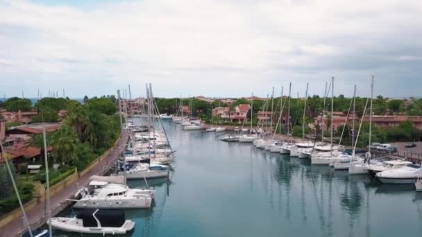 Вид с воздуха на пришвартованные белые парусные лодки в порту Портороса, Фурнари, Италия. Средиземное море и облачное небо. Здания, зеленые деревья — стоковое видео