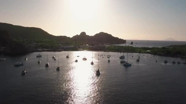 Vista aérea en la costa de la isla de Lipari. Árboles verdes y edificios. Montañas y puesta de sol. Yates, catamaranes y barcos. Sicilia, Italia — Vídeo de stock