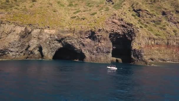 Αεροφωτογραφία σε λευκό σκάφος αγκυροβολημένο κοντά σε σπήλαιο του νησιού Λιπάρι στη Μεσόγειο θάλασσα. Κάποιοι επιβαίνουν στο σκάφος και κάποιοι κολυμπούν. Σικελία, Ιταλία — Αρχείο Βίντεο