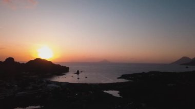 Lipari Adaları 'nda ağaçlar, binalar, dağlar olan hava manzarası. Demirlemiş yatlar ve yelkenli tekneler. Akdeniz, gün batımı. Sicilya, İtalya