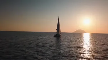 Akdeniz 'de Lipari Adası' na karşı yüzen beyaz yelkenlinin hava manzarası. Güneş su yüzeyine yansıyor, güneş doğuyor. Sicilya, İtalya